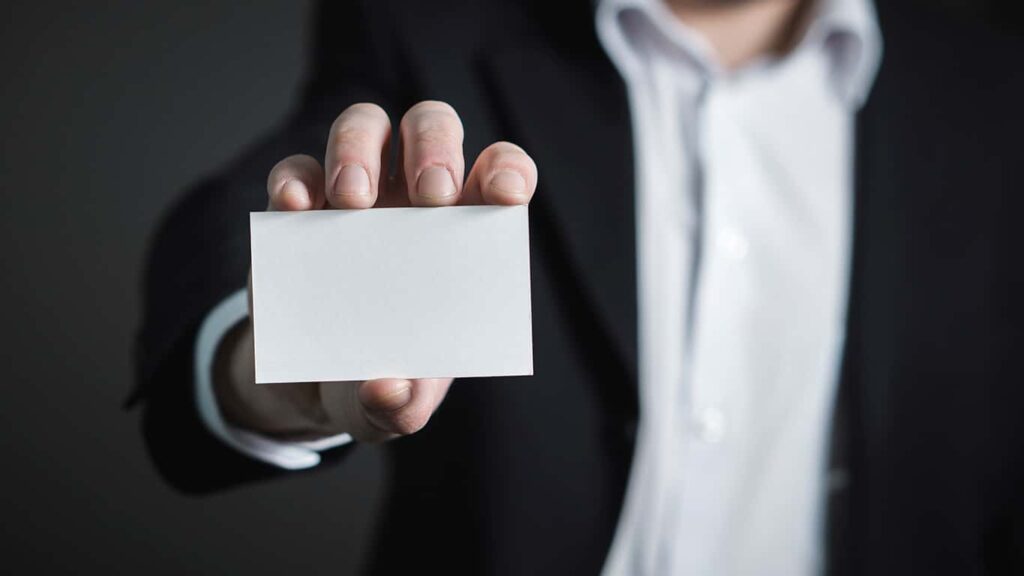 Um homem de roupa social segura um cartão de visitas em branco, como se estivesse se apresentando, simbolizando as apresentações que ocorrem depois das palestras do MBX. 
