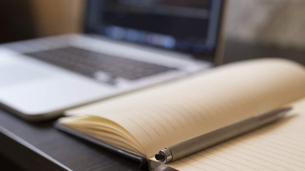 Página em branco de um caderno com linhas e uma caneta posicionados à frente de um notebook, indicando que o profissional pode aprender com o Blog MBA USP/Esalq. 