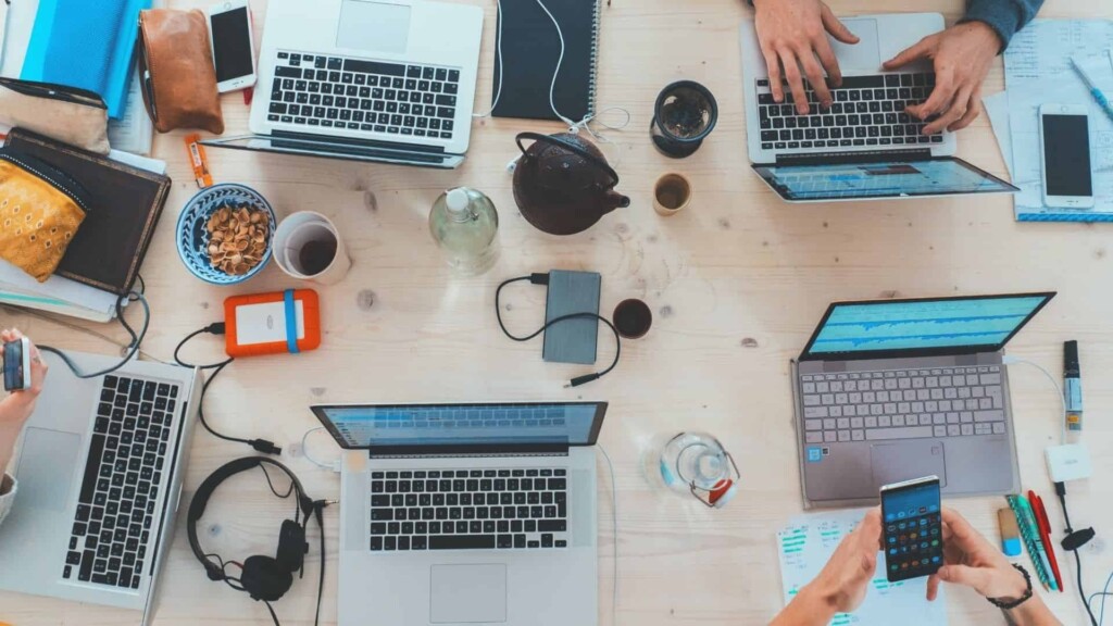 Pessoas que trabalham com Digital Business sentam a uma mesa com vários notebooks, tablets e celulares para trabalhar.