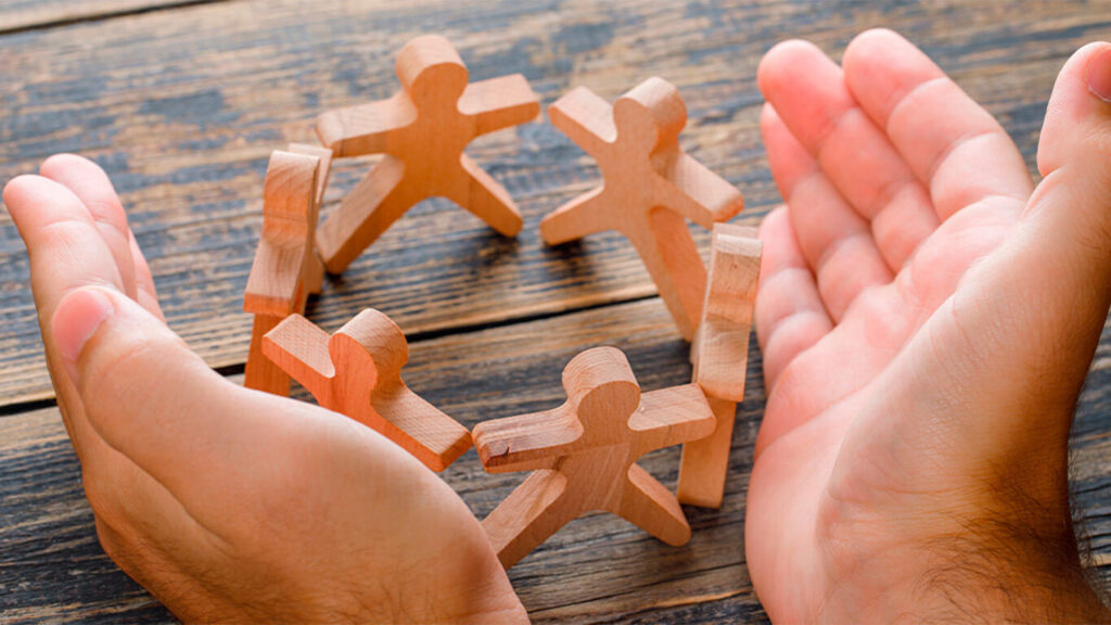 duas mãos em volta de bonequinhos em círculo que representam a aplicação da inteligência emocional para líderes