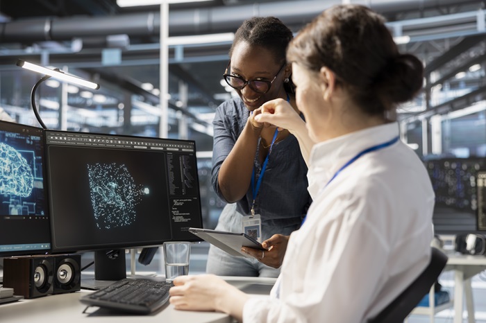 A imagem mostra duas mulheres em um ambiente profissional tecnológico; elas olham para o monitor e comemoram uma implementação de ia para automação.