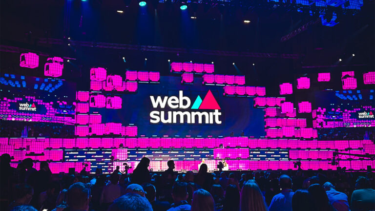 Imagem do telão de uma das salas de palestra do Web Summit, com o logo e luzes roxas.