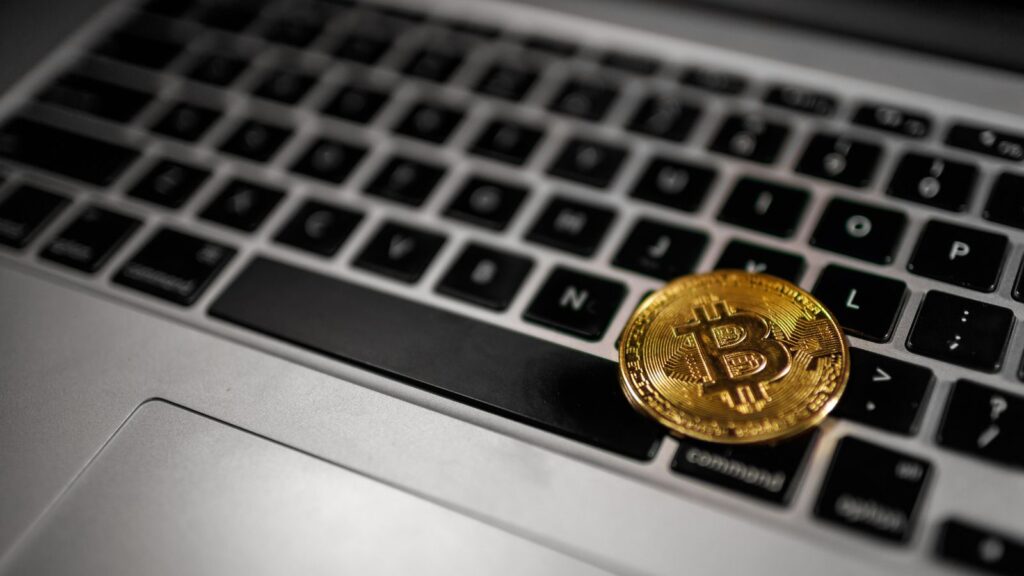 Uma moeda de Bitcoin repousa sobre um teclado de notebook, simbolizando a conexão entre as finanças digitais e a tecnologia blockchain, que está revolucionando o mercado financeiro e as práticas de controladoria nas empresas.
