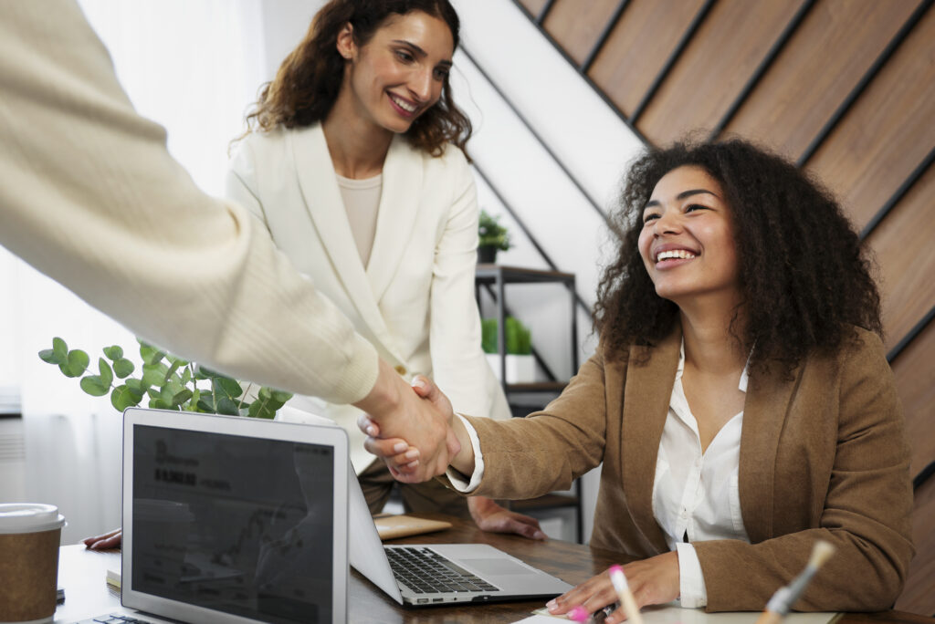 Imagem de um ambiente corporativo onde uma mulher, aperta a mão de outra pessoa, ilustrando o momento de uma negociação ou parceria.