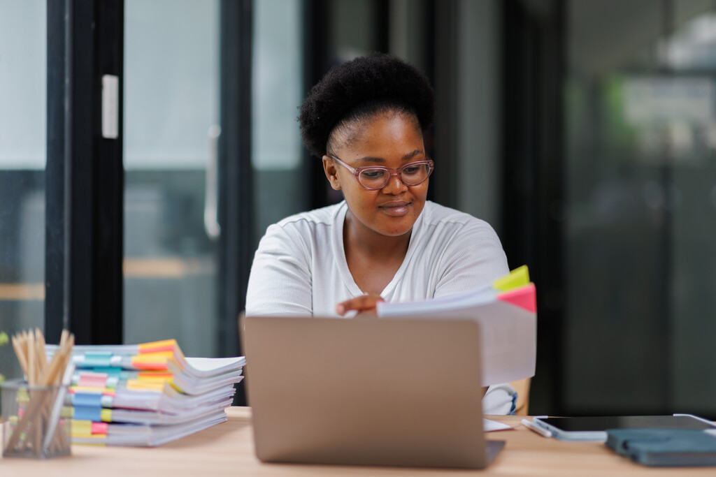Mulher em escritório, sorridente, utilizando notebook para pesquisar o que é MBA em gestão escolar.