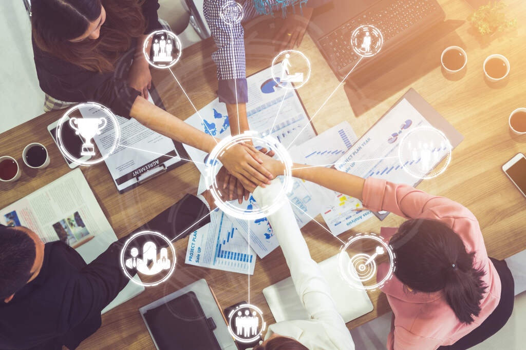 Visão de cima de mãos em conjunto, com diversos ícones digitais flutuando ao redor, representando a delegação de funções.