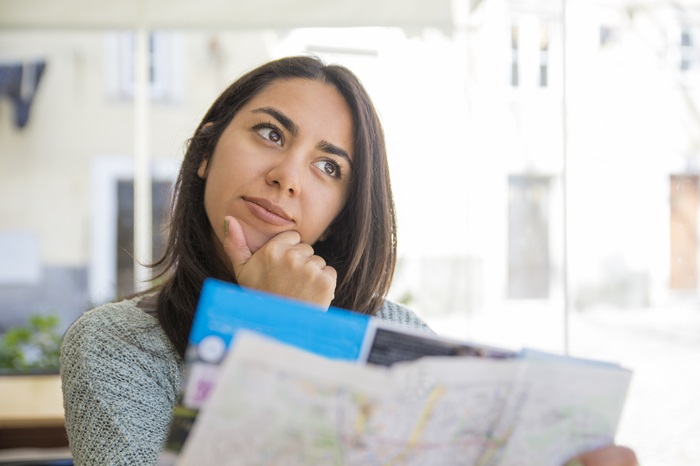 Uma jovem profissional avalia papeis, dentre eles um mapa, com expressão de reflexão e dúvida, como se estivesse estudando as opções para uma decisão importante.