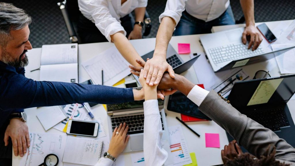 Imagem com pessoas juntando as mãos para mostrar engajamento que é um benefício do mba em gestão de pessoas.